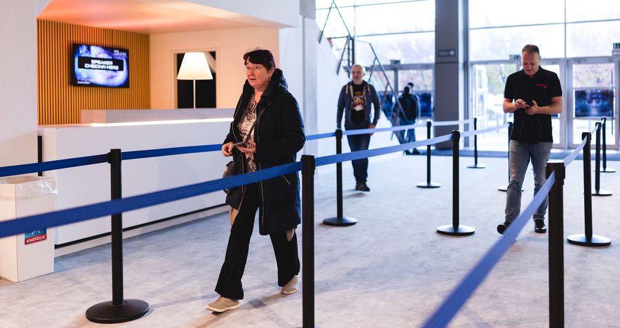The registration area with blue belt barriers, attendees queueing and daylight through the window wall.