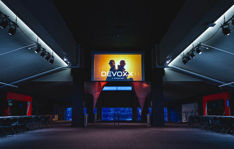 An auditorium from the back row: raked seating, Devoxx artwork on the screen, blue and red wall lighting.