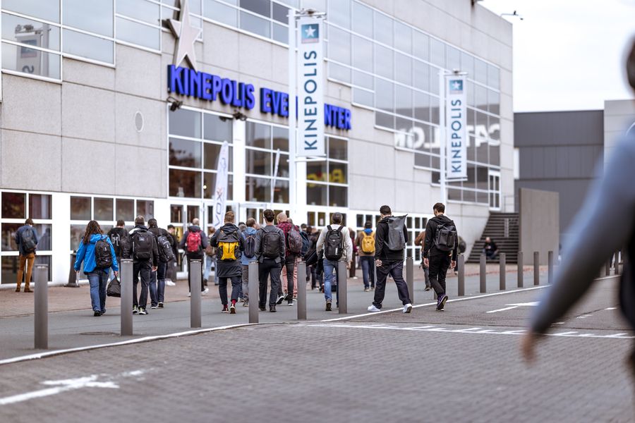 A crowd of attendees walking towards the Kinepolis entrance past Devoxx banners on a bright day.